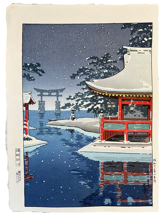 Estampe Japonaise de Koitsu Tsuchiya, paysage d'hiver, temple rouge sous la neige en premier plan, le torii de Miyajima au loin, les pieds dans l'eau; la neige tombe à gros flocons